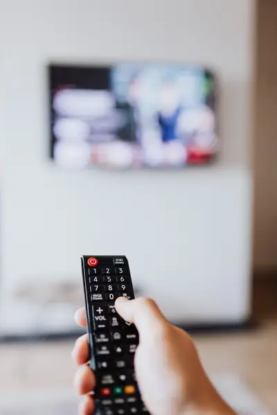 Hand holding a TV remote control pointed at a television